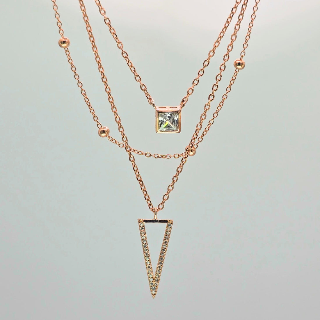 Two rose gold necklaces with gemstone pendants on a light gray background