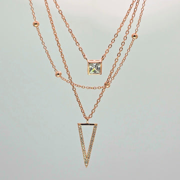 Two rose gold necklaces with gemstone pendants on a light gray background