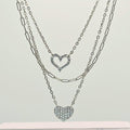 Two silver heart-shaped pendant necklaces on a light gray background