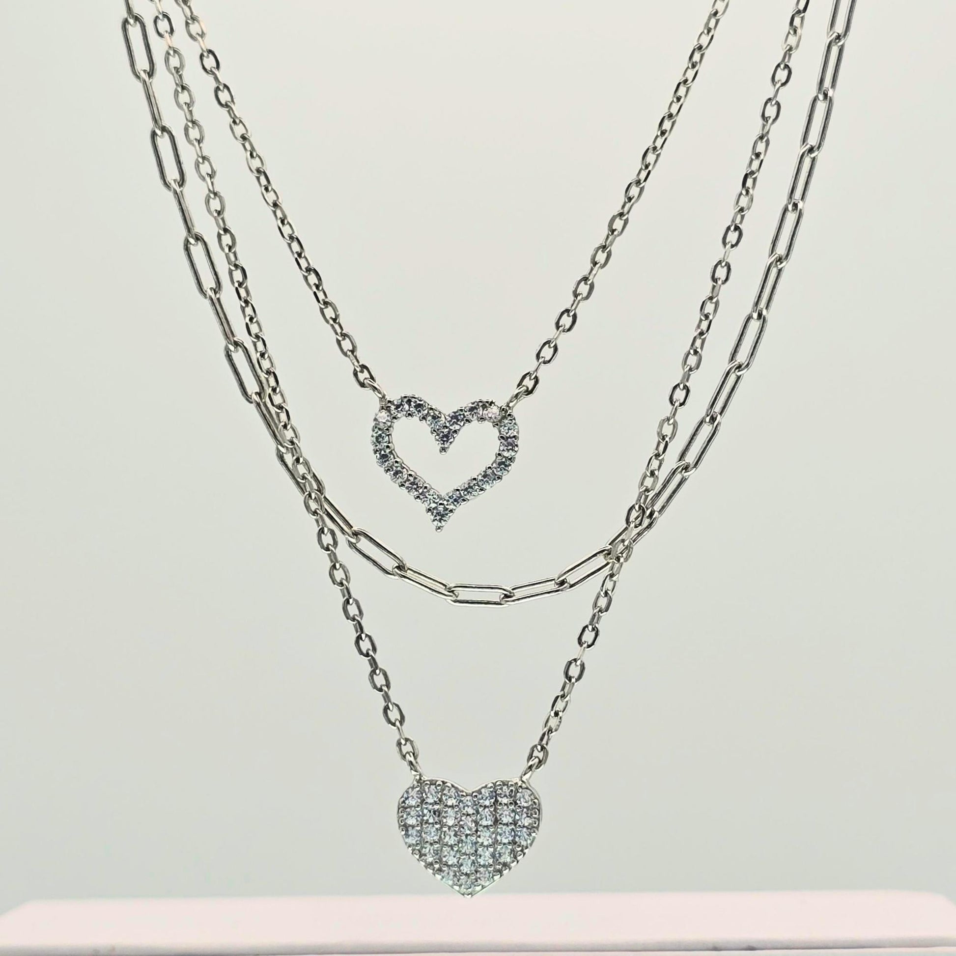 Two silver heart-shaped pendant necklaces on a light gray background