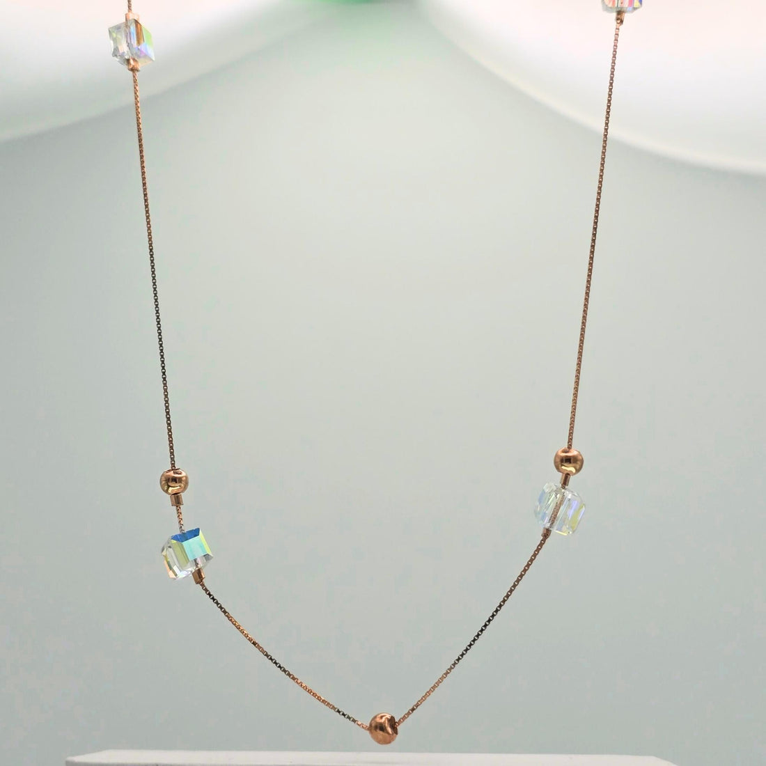 Necklace with rose gold beads and clear crystal-like elements on a light gray background