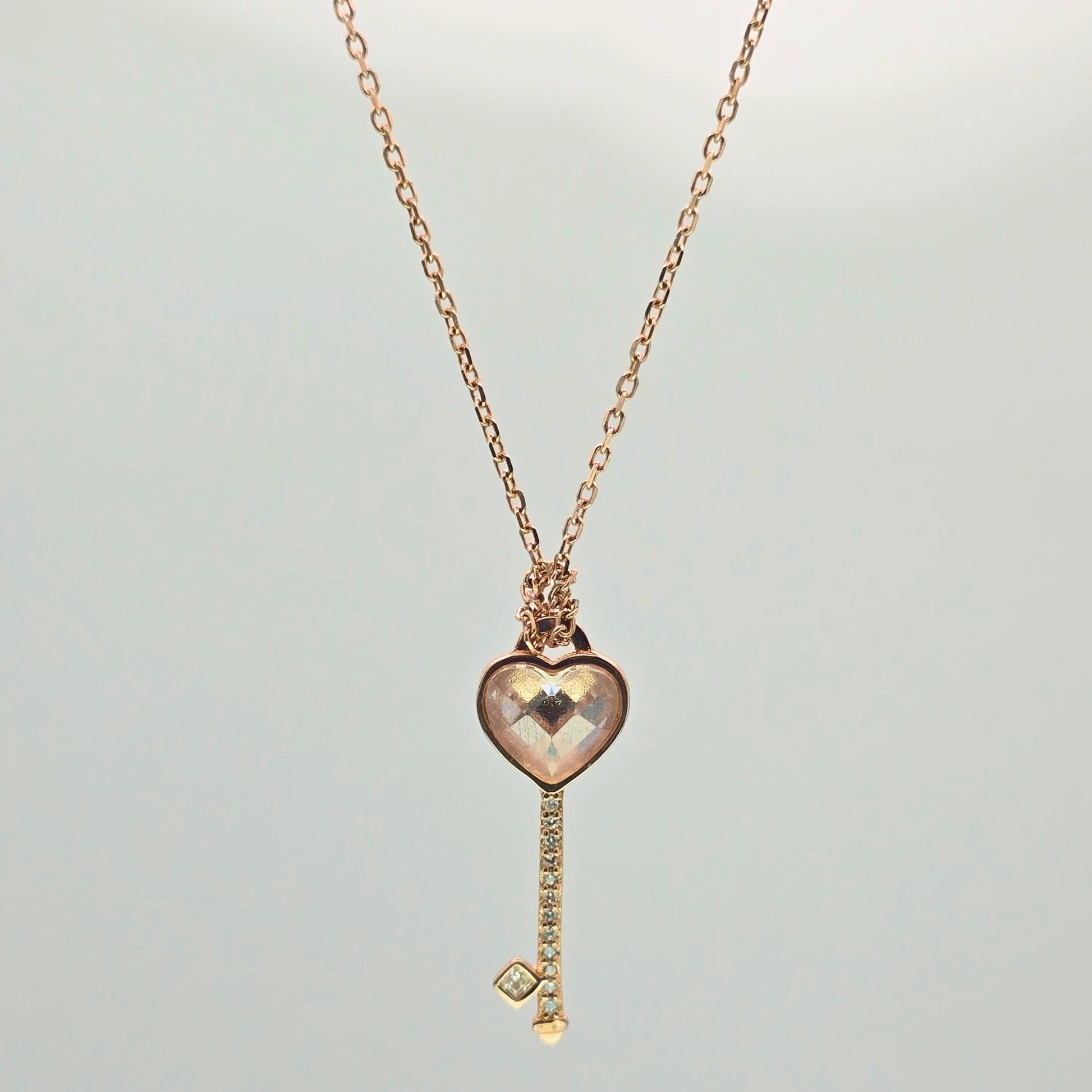 Rose gold heart-shaped key pendant necklace on a light gray background