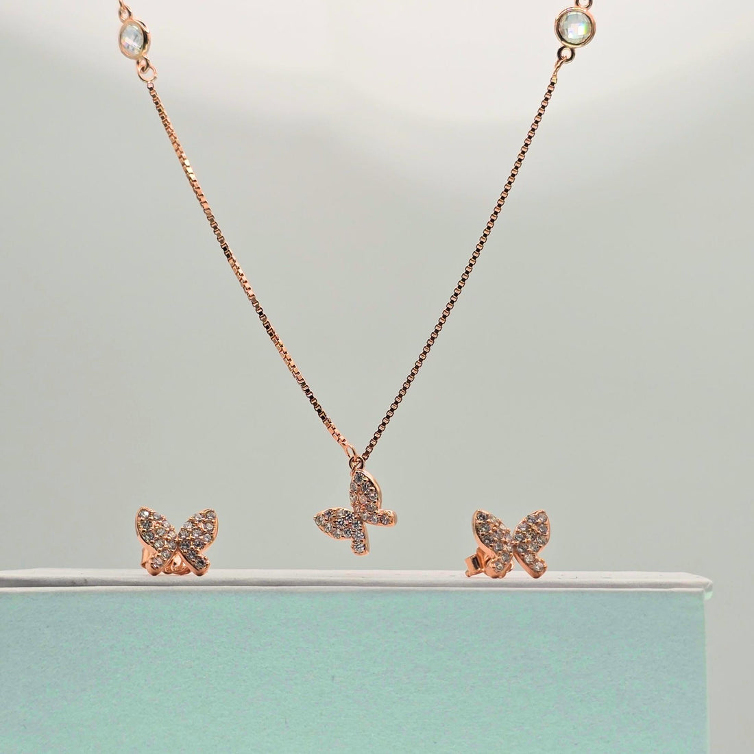 Rose gold butterfly necklace and earrings on a light green background