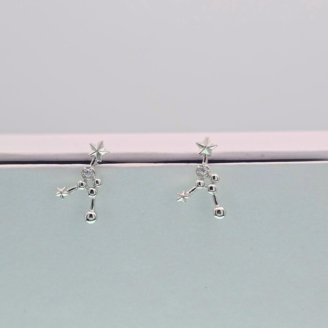 Silver constellation earrings on a light gray background