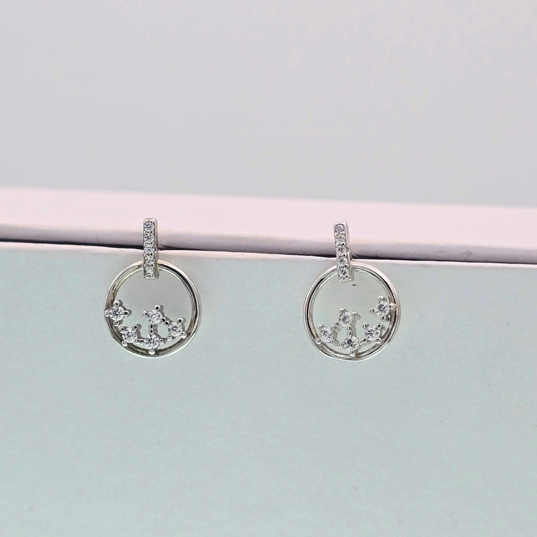 Silver hoop earrings with small diamonds on a light gray surface