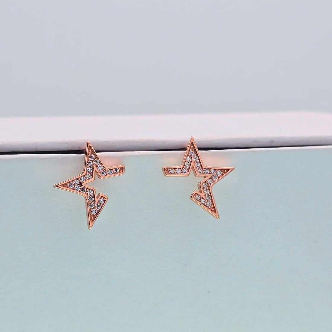 Rose gold star-shaped earrings on a light blue surface