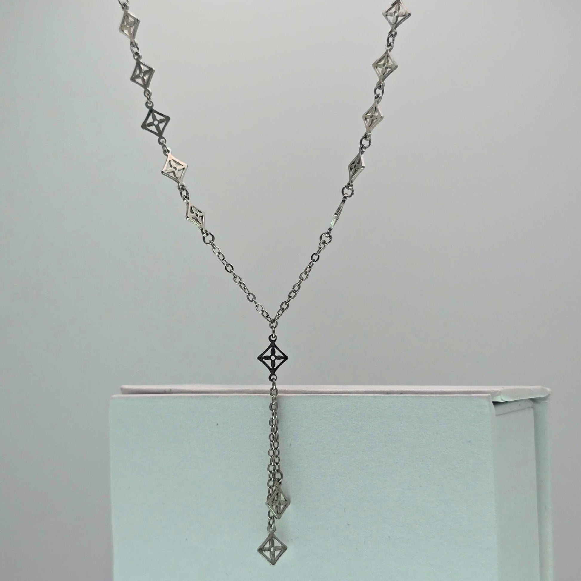 Silver necklace with geometric designs on a light gray background