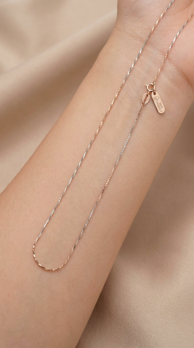 Rose gold necklace on a person's wrist against a beige background