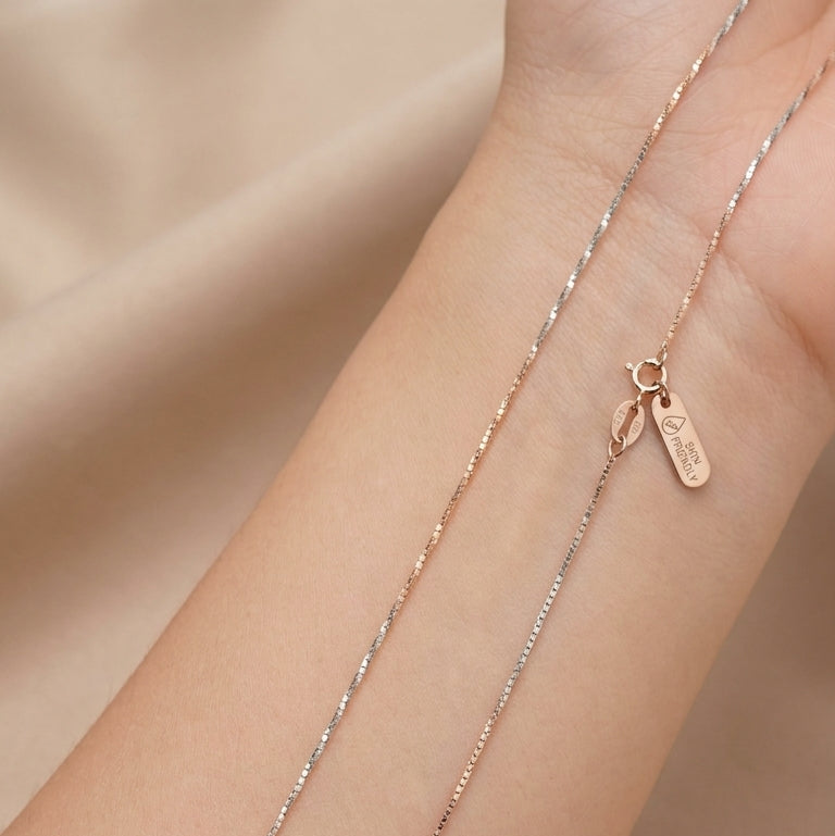 Rose gold necklace on a person's wrist against a beige background