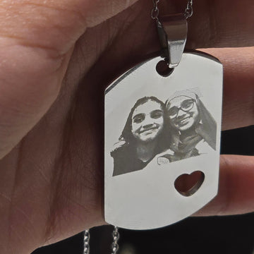 Hand holding a silver dog tag with engraved image, blurred background